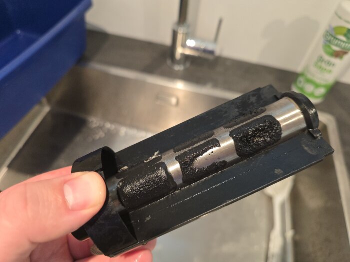 Magnetitfilter med svarta järnspån rengörs i en diskho i tvättstugan. En hand håller filtret under diskning.