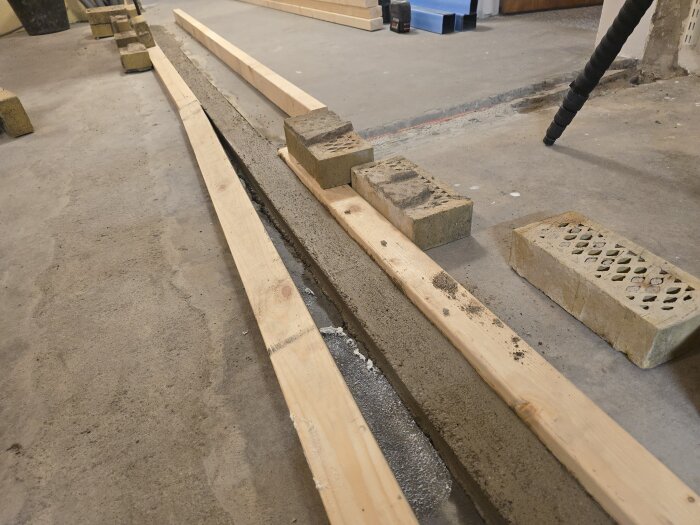 Betonggolv som härdar med träbrädor och tegelblock på golv i renoveringsprojekt.