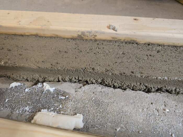 Färsk betong har hällts och formas mellan träreglar på ett golv, med rester av härdad betong och spackel synliga.