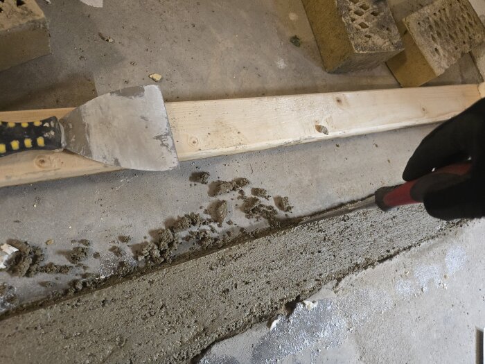 Betong som härdar, en spatel och en träregel syns på bilden. Någon skrapar bort överflödig betong från en nyligen gjuten yta.