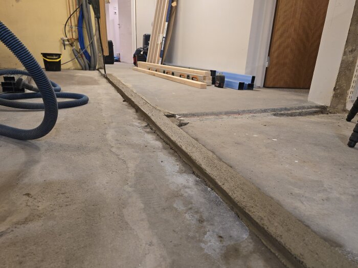 Nyhärdad betongplatta i ett maskinrum, omgiven av verktyg och byggmaterial för en innerväggsrenovering.