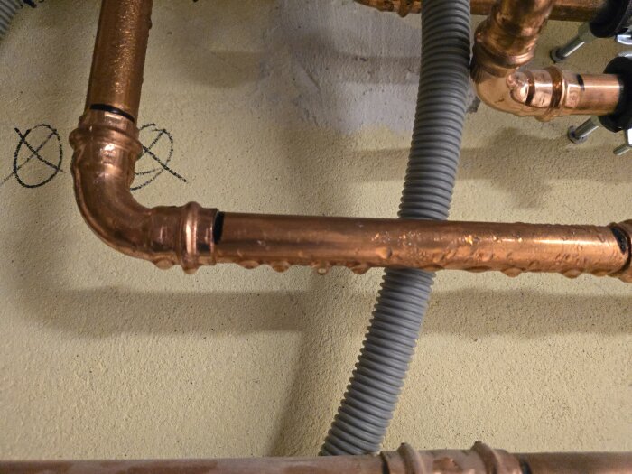 Kondens på kopparrör i tak, bredvid gråa vp-rör. Droppar syns tydligt på rören, vilket indikerar golvvärmesystemets funktion.