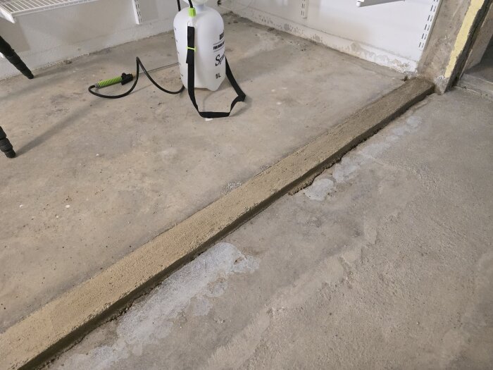 Nylagd betongkant på golv som håller på att härda, med en tryckspruta bredvid för att blöta betongen under byggprojekt.