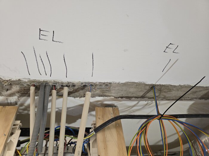 VP-rör och flexrör går genom tak med märkningar "EL" för elkablar, synliga kablar hänger ner från bjälklaget i renoveringsprojekt.