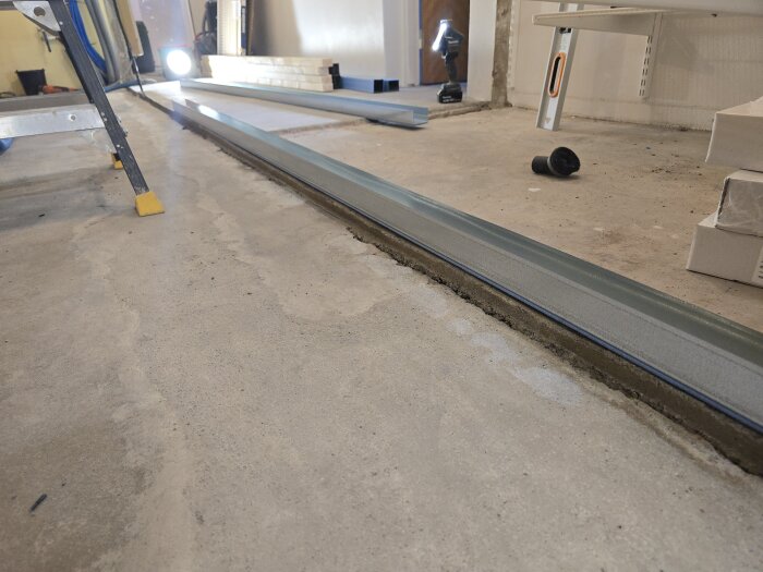Stålregel placerad på gjutet betonggolv, med byggmaterial och verktyg synliga i bakgrunden.