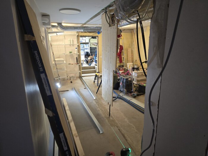 Renoveringsarbete pågår i ett rum med synliga stålreglar, byggmaterial, och verktyg. En grön laserlinje hjälper till med mätning och placering.