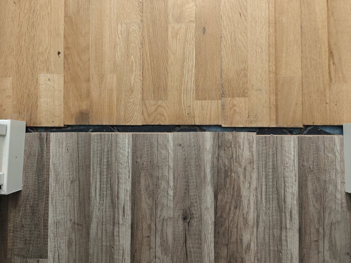 Skarv mellan ett ljust trägolv och ett mörkt klinkergolv med synlig betong mellan, en konstruktion söks för att täcka skarven.