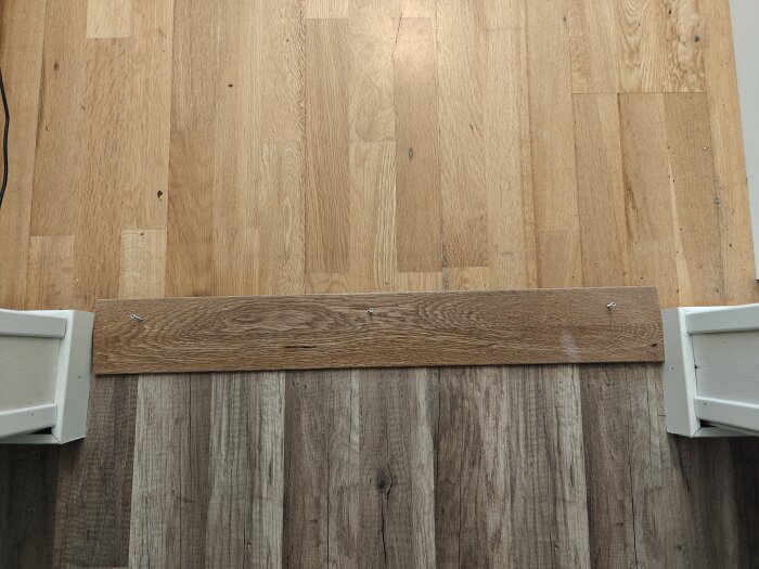 Trägolv möts av klinkerplattor med en trälist som skarv, fäst med skruvar vid golvet.