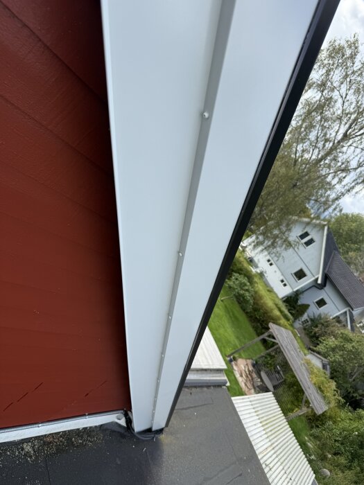 Vit takfotsinklädnad på ett rött hus, trädgård i bakgrunden.