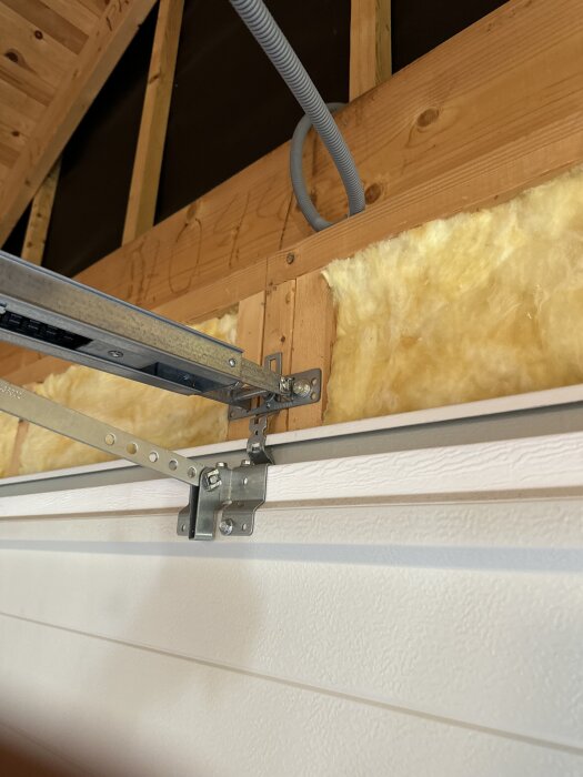 Isolerat garage med monterad port, visande fästen och metallstöd monterade på trästomme med synlig gul isolering.