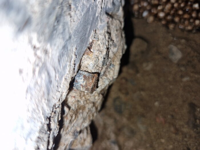 Rostig armering syns i del av betongvägg, oskyddad och delvis exponerad med grov struktur runtomkring.