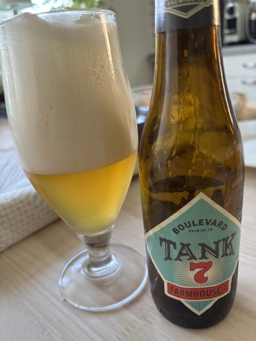 Ett glas med belgisk öl och en flaska Boulevard Brewing Co. Tank 7 Farmhouse Ale på ett bord.