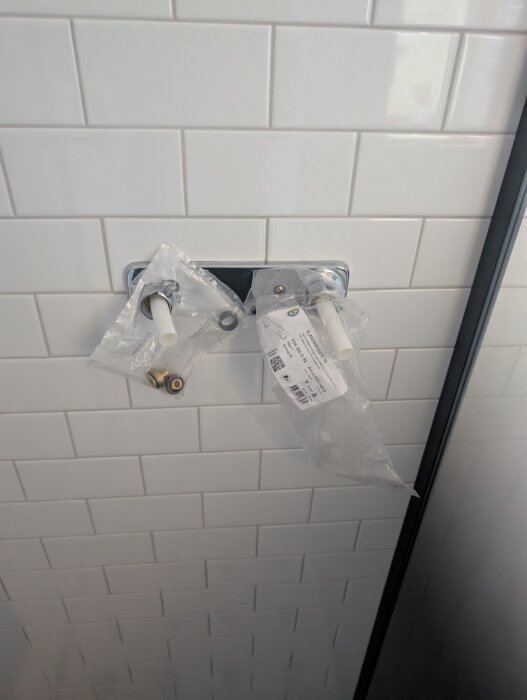 Blandarfäste och väggbrickor monterade på kakelvägg med anslutna rör i plastförpackningar.