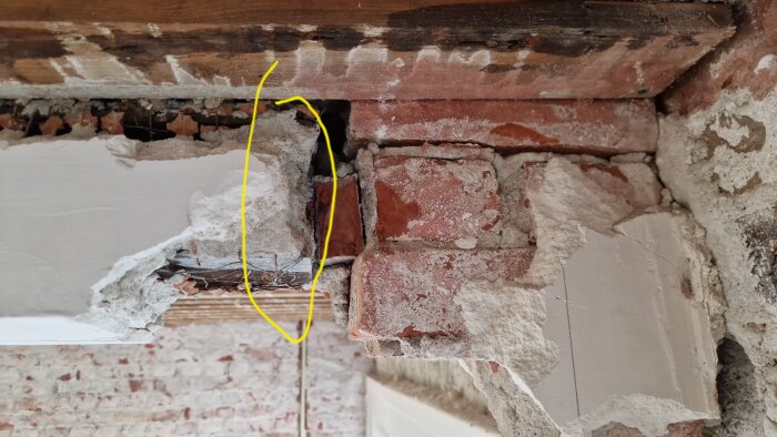 Murverk med synligt tegel och skador i putsen, markerat med gul linje för att visa var arbetet ska utföras.