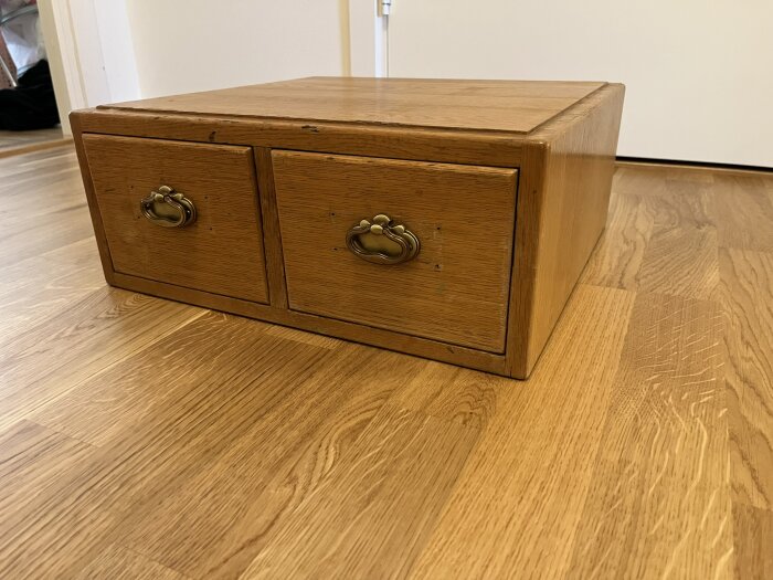 Trälåda med två lådor och metallhandtag som behöver repareras; lådfronterna har delvis lossnat.