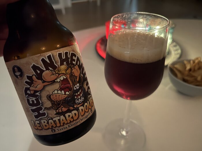 Flaska med etiketten "Herman Hedning Le Bâtard Double" från Vreta Kloster Bryggeri, bredvid ett glas med mörkt öl på bordet.