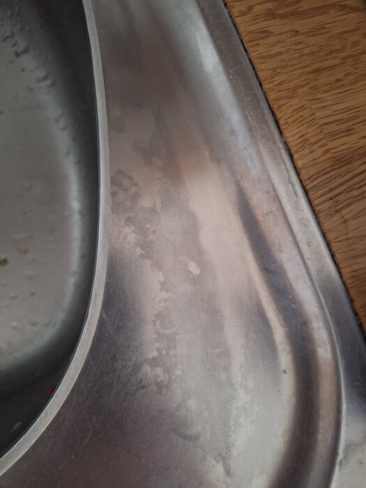 Missfärgad diskbänk i rostfritt stål med rengöringsfläckar på ytan.