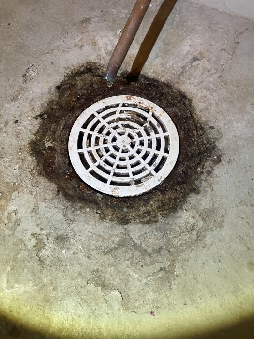 Rostig golvbrunn i betonggolv nära en elpanna med tydliga kondensspår runt brunnen.