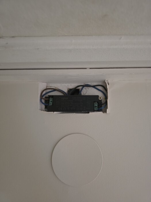 En transformator synlig i en öppning ovanför en dörr, monterad i en vägg med sladdar omkring, utanför ett badrum.