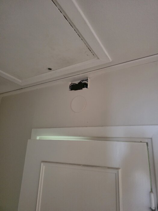 Transformator infälld i väggen ovanför en dörr utanför badrummet, med synliga kablar och monteringshål.