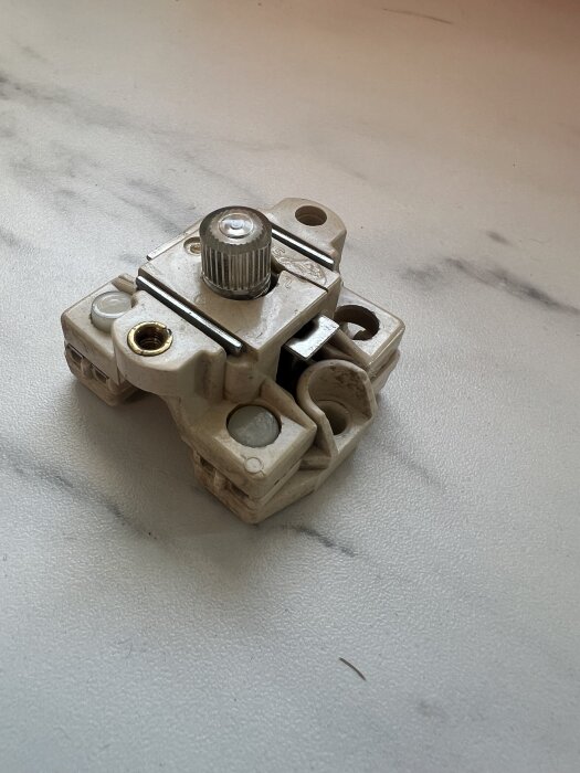 Elektrisk porslinssäkring med synlig metallskruv på vit yta.