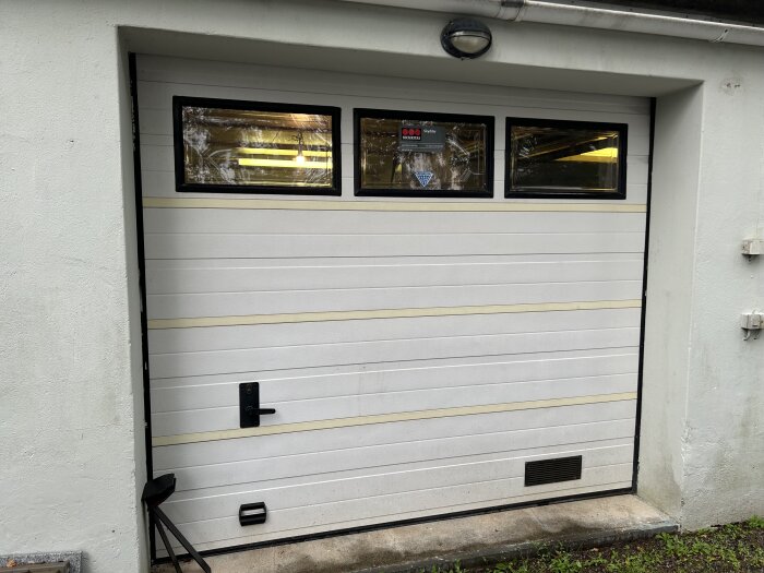 Vit garageport med tre fönster upptill, omgiven av vit fasad.