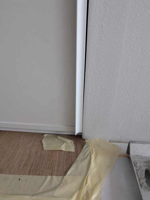 En skjutdörr med synligt glapp mellan dörr och gipsvägg. Tejp och hörnlist syns, vilket tyder på byggarbete.
