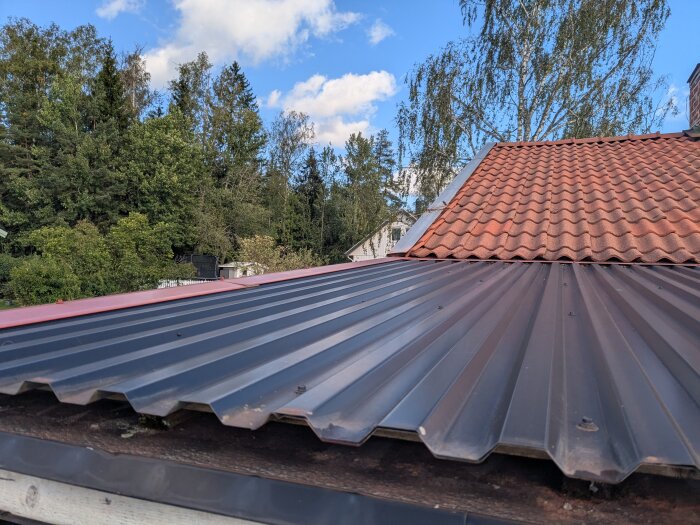 Tak med korrugerad metallplåt och tegelpannor, omgivet av träd. Fråga om täta mot en metallskorsten.