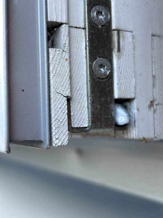 Detalj av fönsterkarm med spanjolett; den går endast in i nedre delen av ramen, med synliga sprickor i det vita träet.