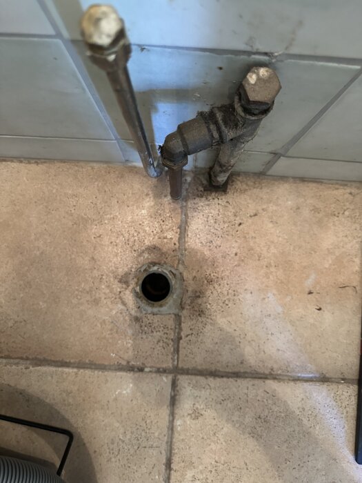 Avloppsbrunn i kaklat golv med intilliggande rör i en liten tvättstuga.