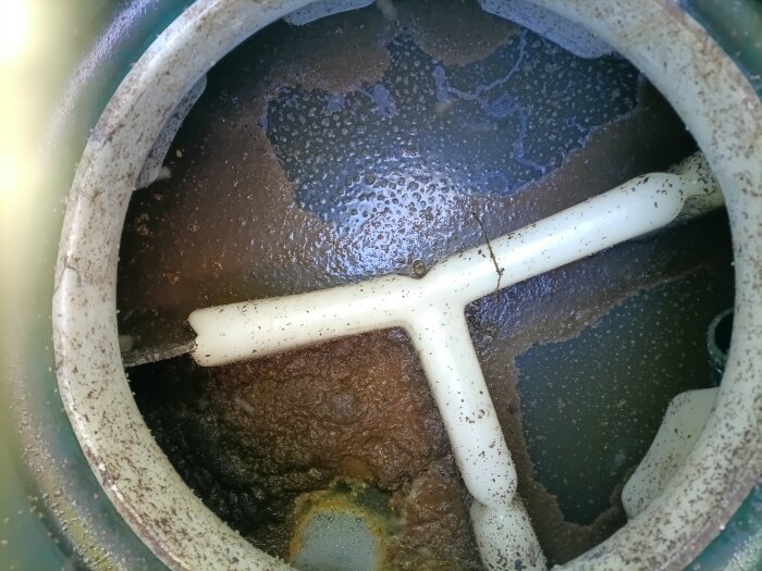 Inuti en slamavskiljare med korroderade ytor och smutsigt vatten. Tre vita rör syns, en del av systemets avlopp eller ventilation.