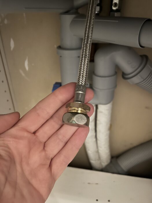 Hållande en flexibel metallslang under diskho med avloppskopplingar och rör.