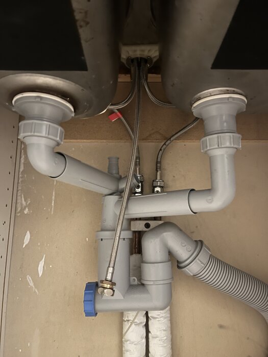 Rör och installationer under diskhon med plats för bänkdiskmaskin i hyresrätt.