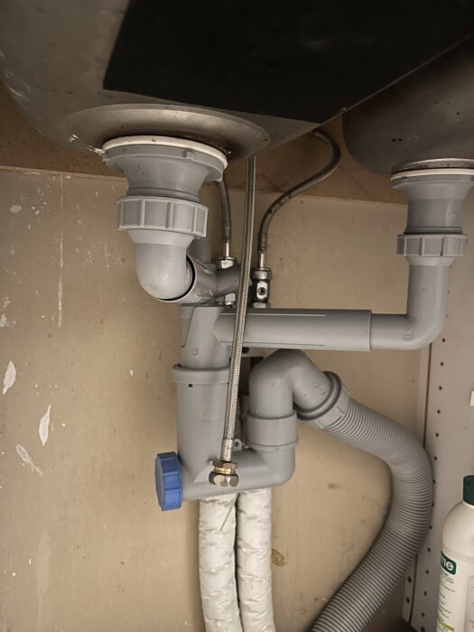 Pipes and plumbing under a kitchen sink, showing drainage setup and preparation for water and drain connections.