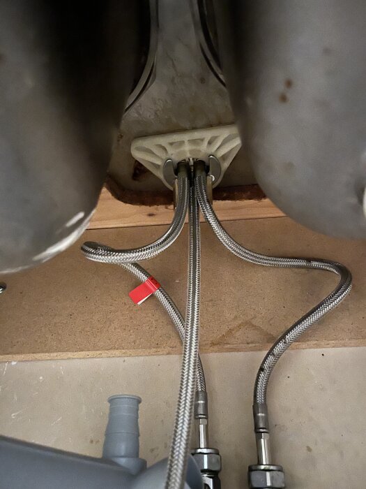 Vatten- och avloppsrör under diskbänken, med synliga kopplingar och slangar redo för installation av bänkdiskmaskin.