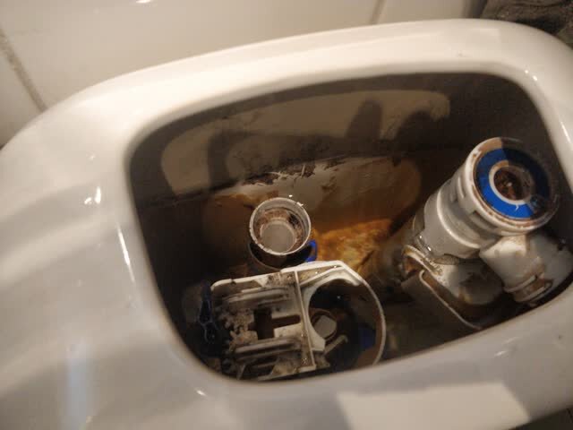 Toaletttank med trasig spolningsanordning, saknade delar synliga.