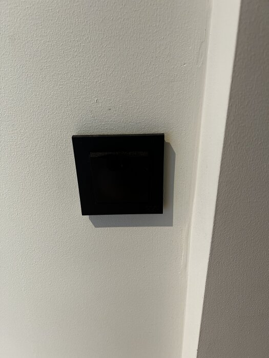 Svart Elko Plus knappdimmer monterad på en vit vägg.
