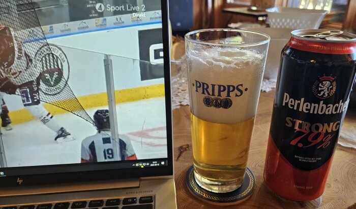 Dator visar livesänd hockeymatch, bredvid ett glas öl och en burk Perlenbacher Starköl med 7,9% från Lidl på ett bord.