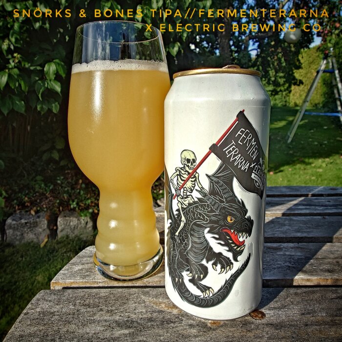 Burk med ölliknande dryck från Fermenterarna, design med drake och skelett, bredvid glas med gyllene dryck, utomhus.