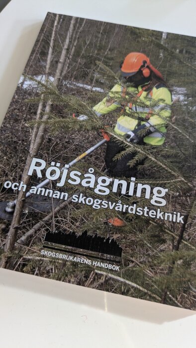 Person i skogsröjningsutrustning använder röjsåg i skog. Boken heter "Röjsågning och annan skogsvårdsteknik".