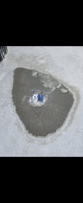 Betongplatta med en stor vattenpöl på ytan, ett område med våt cement runt en blå och vit etikett i mitten.