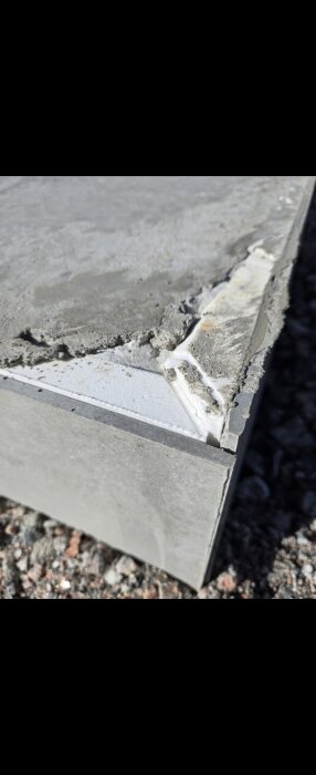 Nylagd betongplatta med synliga ojämnheter och en exponerad kant av underliggande material, fotograferad på en grusig yta.