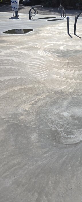 Betongplatta med vattenpölar och märken från gjutning, kablar i bakgrunden.