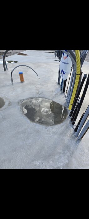 Betongplatta med synliga vattenpölar och flera utstickande rör, potentiellt konstruktioner för el eller vattenanslutningar.