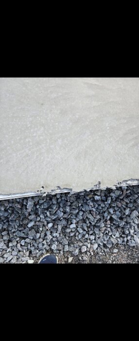 Kant av nylagd betongplatta med stenar och en skymt av en sko närvarande.