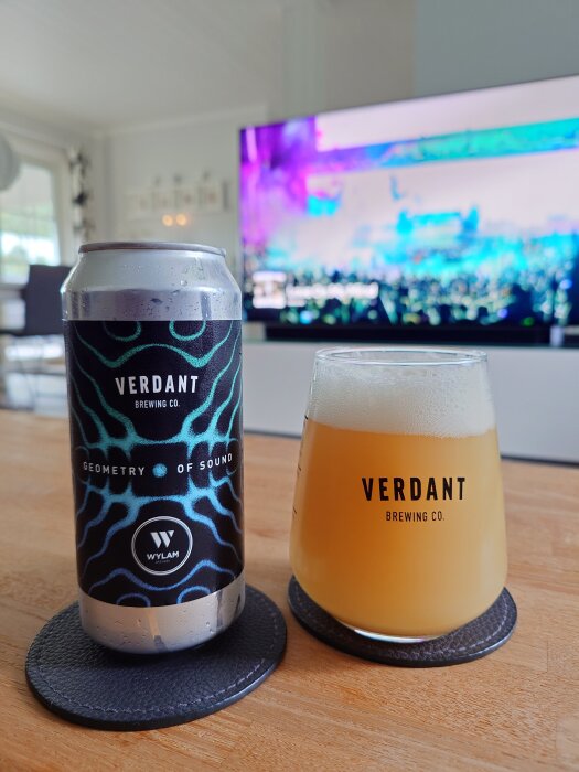 Burk och glas med Verdant Brewing Co., etikett "Geometry of Sound." Bakgrund: TV-skärm med färgglatt motiv.
