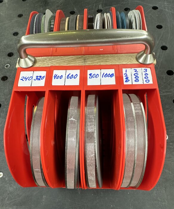 Röda förvaringsfack innehållande slip- och diamantskivor märkta med grit-nummer från 240 till 3000, med ett handtag ovanpå.
