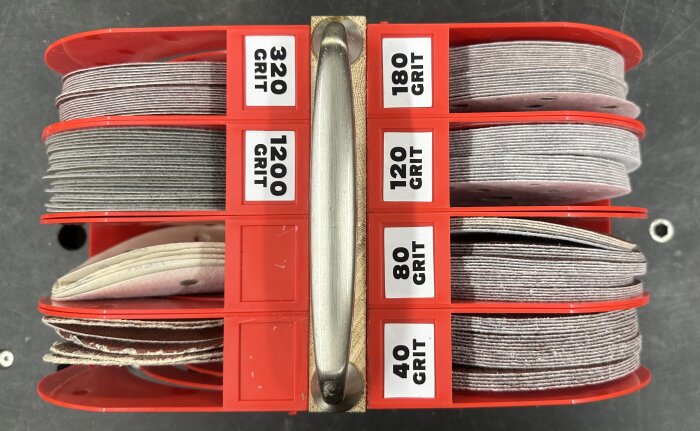 Röda plastfack fyllda med sliprondeller i olika grovlek: 40, 80, 120, 180, 320, 1200 GRIT, organiserade för slipmaskiner.