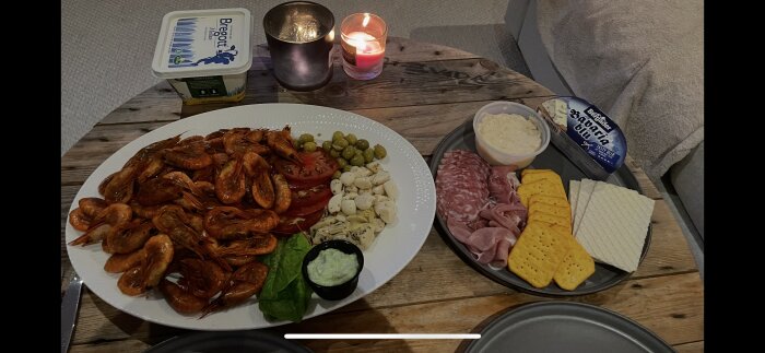 Egenrökta räkor med oliver, mozzarella, salami, skinka, kex och dippsåser på ett träbord med ljus och smörpaket.