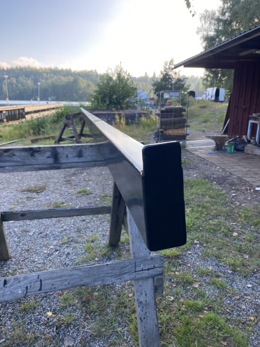 Svartmålat rör på sågbockar utomhus, omgiven av grönska och trähus, del av byggprojekt för hamnbom.